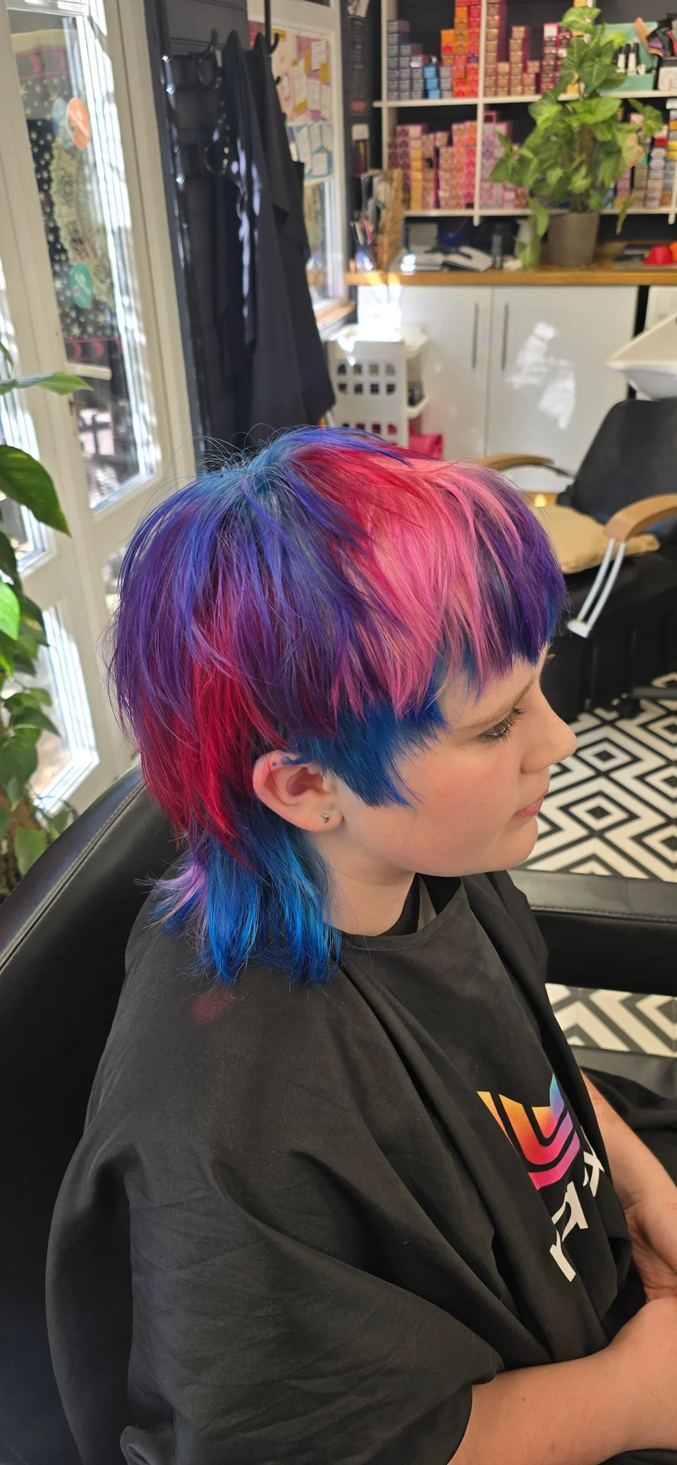 Short pixie haircut in vivid blue, purple and pink, viewed from the side